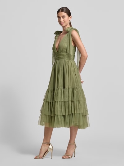 Frauenmodel trägt Knielanges Kleid mit Rüschenbesatz von LACE & BEADS in Oliv, Mesh, Taillierte Passform, Ärmelloses-Design, V-Ausschnitt, Zierschleife, Ganzkörperansicht von vorne.