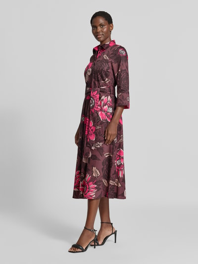 Frauenmodel trägt Midikleid aus reiner Baumwolle von Christian Berg Woman mit floralem Allover-Print in Braun und Pink, Ganzkörperansicht von vorne. Taillierte Passform, Umlegekragen, integriertes Taillienband, 1/2-Arm, glatte Textur, Rückenlänge 123 cm, Brustweite 50 cm, Ärmellänge 47 cm.