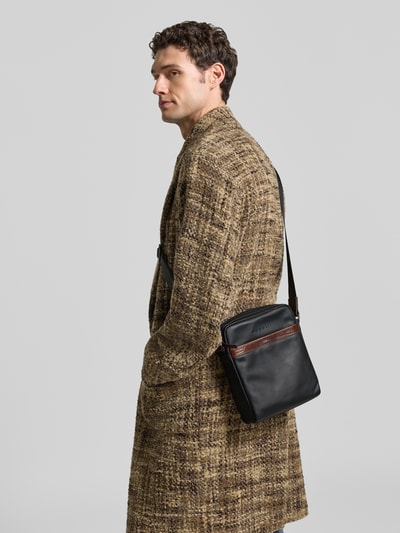 Männermodel trägt Umhängetasche mit Label-Detail Modell 'Corso Deluxe' von bugatti in Schwarz mit braunem Akzent, Ganzkörperansicht Rückansicht. Hauptfach mit Reißverschluss, verstellbarer Schulterriemen, Größe 22x27x8 cm, Länge Riemen 90 cm.