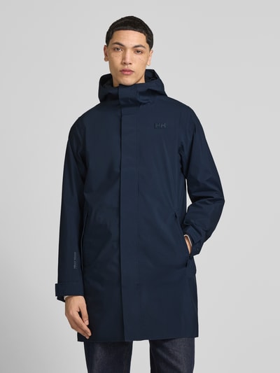 Mężczyznamodel nosi Regular Fit Regenmantel mit Logo-Detail Modell 'Brussel' od Helly Hansen, granatowy, wpuszczane kieszenie, kaptur ze stójką, długość tyłu w rozmiarze M 90 cm, szerokość ramion w rozmiarze M 42 cm, szerokość klatki piersiowej w rozmiarze M 51 cm, długość rękawów w rozmiarze M 68 cm, Ganzkörperansicht z przodu.