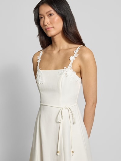 Frauenmodel trägt Cocktailkleid aus Leinen-Viskose-Mix von Forever New, cremefarben, schmale Träger mit Blumen, Taillenband, Nahaufnahme Oberkörper.