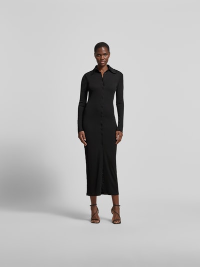 Frauenmodel trägt Hemdblusenkleid in Maxilänge von Nanushka, schmal geschnitten, Hemdblusenkragen, durchgehende Knopfleiste, langärmelig, Schwarz, glatte Textur, Ganzkörperansicht von vorne. Gesamtlänge bei Größe S: 134 cm, Brustweite: 40 cm, Ärmellänge: 64 cm