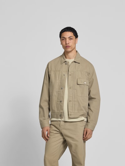 Männermodel trägt Jeansjacke aus reiner Baumwolle von Forét in Beige, Regular-Fit, Durchgehende Knopfleiste, Brusttasche, Umlegekragen, Ganzkörperansicht von vorne. Rückenlänge bei Größe M: 64 cm, Schulterbreite 49 cm, Ärmellänge 64 cm.