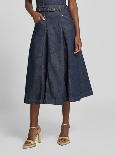 Frauenmodel trägt Jeansrock mit Gürtel Modell 'RAYNE' von GUESS aus dunkelblauem Baumwoll-Mix in A-Linie, Ganzkörperansicht von vorne.