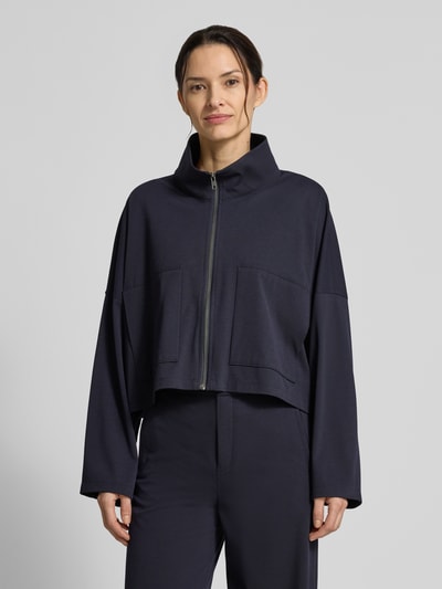 Vrouwenmodel draagt Relaxed Fit blazer met viscose van Drykorn, elastische materiaalmix, opstaande kraag, ritssluiting, opgestikte zakken, model 'Elstow', donkerblauw, gladde textuur, voorkant bovenlichaam close-up.