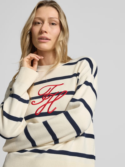 Vrouwenmodel draagt Regular Fit Sweatshirt uit puur katoen van Tommy Hilfiger, fijngebreid, all-over motief, gestreept patroon, gestikt logo, ronde hals, lange mouw, rompzoom en mouwboorden geribd, crème met donkerblauwe strepen, zachte textuur. Close-up bovenlichaam.