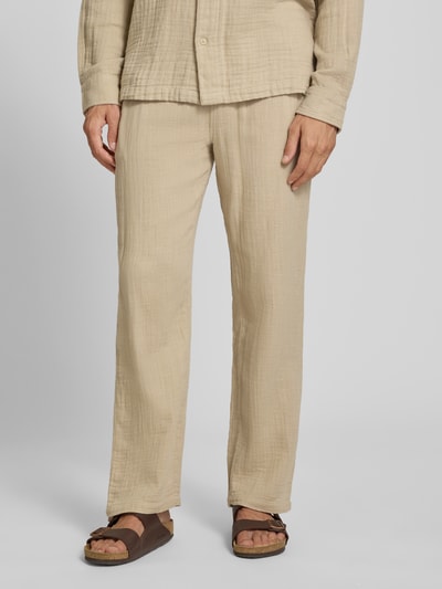Męski model nosi Straight Fit Sweatpants in Musselin-Optik von Lindbergh, spodnie dresowe z bawełny, kolor beżowy, struktura muślinu, elastyczny pas z tunelem, szerokość w rozmiarze M 41 cm, długość wewnętrzna nogawki 81 cm, ganzkörperansicht von vorne.