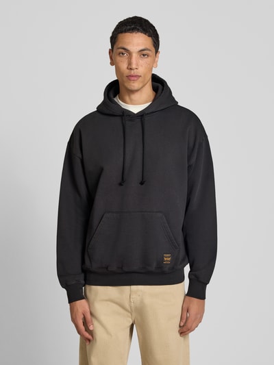 Männermodel trägt Relaxed Fit Hoodie aus Baumwoll-Mix Modell 'JET BL' von Levi's® in Schwarz, beige Hose, Ganzkörperansicht von vorne.