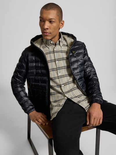 Męski model nosi Kurtka pikowana z zamkiem błyskawicznym dwustronnym Model 'Charles' od Blauer Usa, krój regular fit, kaptur, detal z logo, długość tyłu w rozmiarze M 65 cm, szerokość ramion w rozmiarze M 47 cm, szerokość klatki piersiowej w rozmiarze M 55 cm, długość rękawów w rozmiarze M 65 cm, kolor czarny, faktura pikowana, całkowity widok od przodu.
