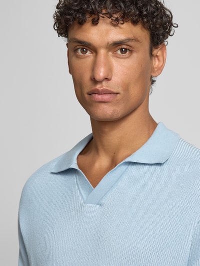 Männermodel trägt Regular Fit Poloshirt aus reiner Baumwolle Modell 'ARAVOLO' von BOSS Orange in Strickoptik mit Label-Patch, Nahaufnahme Oberkörper.