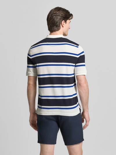 Männermodel trägt Slim Fit Poloshirt mit Logo-Stitching von Gant aus reiner Bio-Baumwolle, dunkelblau-weiß gestreift, Ganzkörperansicht Rückansicht.