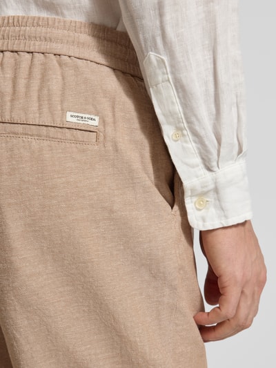 Männermodel trägt Shorts aus Baumwoll-Leinen-Mix mit elastischem Bund von Scotch & Soda, beigefarbene Textur, Nahaufnahme Hüfte seitlich, Regular Fit, Tunnelzug, Bundweite 43 cm, Innenbeinlänge 20 cm.