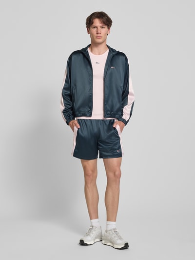 Männermodel trägt Schimmernde Trainingsjacke mit Label-Stitching von BLKVIS, Herren Regular-Fit, Stehkragen, Reißverschluss, Ganzkörperansicht von vorne.