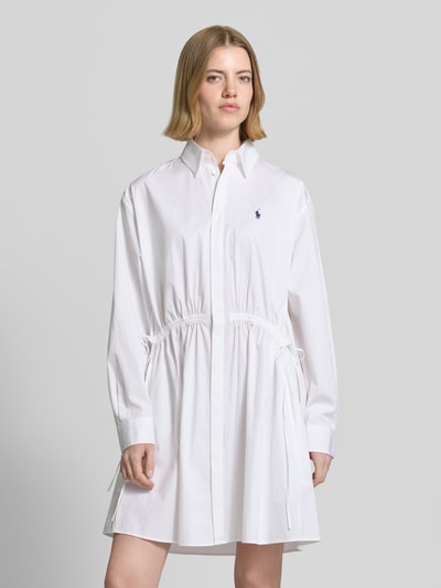 Frauenmodel trägt Tailliertes Hemdblusenkleid aus reiner Baumwolle von Polo Ralph Lauren in Weiß, unifarben, Mini-Länge, mit Hemdkragen, Logo-Stitching und Taillenraffung, Ganzkörperansicht von vorne.