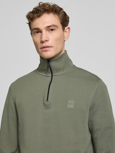 Męski model nosi Regular Fit Troyer aus reiner Baumwolle Modell 'TERRY' od BOSS Orange, zielony, jednolity, materiał sweat, długi rękaw, prosty kołnierz troyer, label patch, krótki zamek, krój regular fit, bawełna, zbliżenie górnej części torsu.