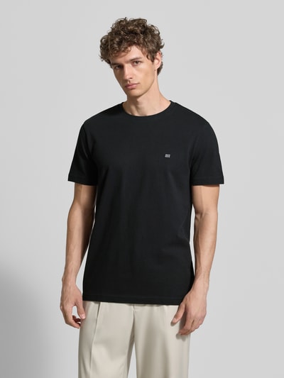 Männermodel trägt T-Shirt aus Baumwolle mit Rundhalsausschnitt von Christian Berg Men in Schwarz, Regular-Fit, Label-Detail, Ganzkörperansicht von vorne.