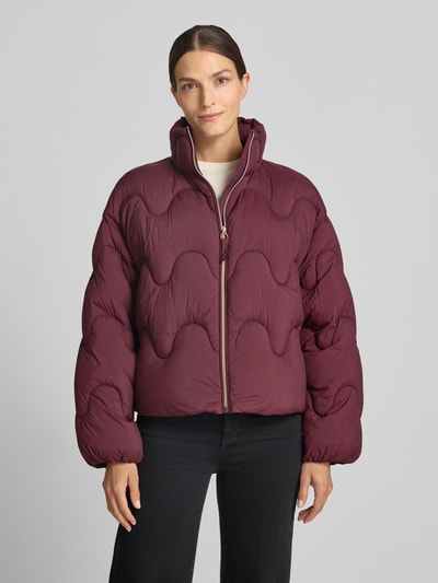 Frauenmodel trägt Loose Fit Steppjacke mit Stehkragen von Jake*s Casual, unifarben in Dunkelrot, mit Reißverschluss, überschnittenen Schultern, langarm, elastischem Ärmelabschluss, Tunnelzug am Rumpf und Eingrifftaschen, Ganzkörperansicht von vorne.