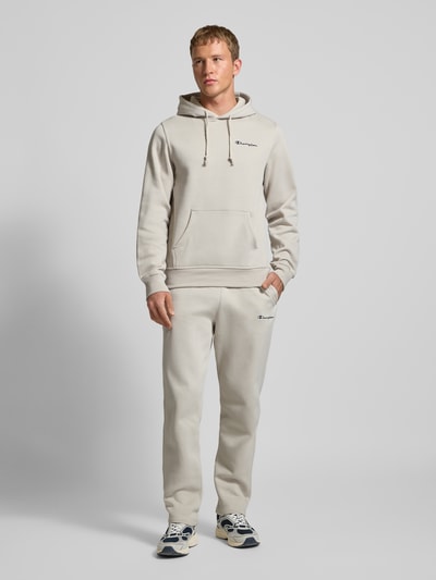 Männermodel trägt Hoodie mit Kapuze von CHAMPION in Creme, Baumwoll-Mix, Lockerer-Schnitt, Kapuze, Tunnelzug, Label-Stitching, Känguru-Tasche, Gerippte-Abschlüsse, Rückenlänge 70 cm, Ärmellänge 70 cm, Ganzkörperansicht von vorne.