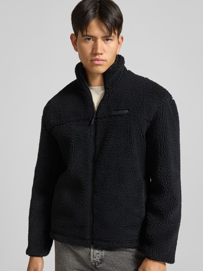 Männermodel trägt Fleecejacke mit Label-Detail und Reißverschluss von REVIEW in Schwarz, Teddyfell-Textur, Ganzkörperansicht von vorne.