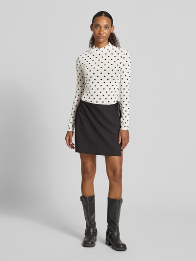 Vrouwenmodel draagt wit shirt met lange mouwen met zwart all-over motief, Slim Fit Langarmshirt mit Allover-Muster Modell 'JESHI' van PIECES, Dames, zwart rokje, zwarte laarzen, Ganzkörperaanzicht van voren.