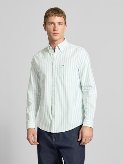 Männermodel trägt Regular Fit Freizeithemd aus reiner Baumwolle von Tommy Jeans mit Optik:Allover-Muster und Logo-Stitching, Ganzkörperansicht von vorne.