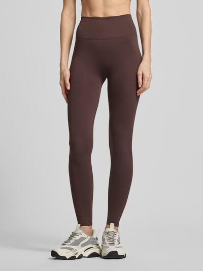 Frauenmodel trägt Leggings mit Logo von aim'n aus braunem Material-Mix mit Stretch-Anteil, elastischer Bund, körpernahe Passform, Ganzkörperansicht von vorne.