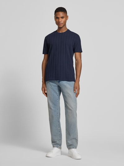 Męski model nosi Regular Fit T-Shirt aus Baumwolle od Guess, czysta bawełna, krój regular fit, okrągły dekolt, detal z logo, długość tyłu w rozmiarze M: 69 cm, pełny widok z przodu.
