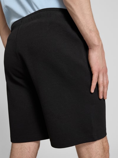 Männermodel trägt Shorts mit Label-Stitching mit elastischem Bund von CHAMPION, schwarz, Baumwoll-Mix, Ganzkörperansicht Rückansicht.