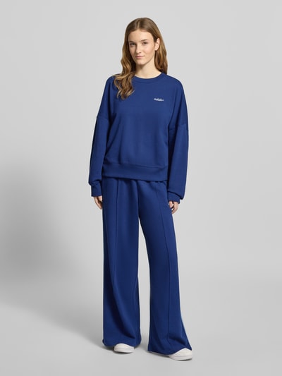 Modelka nosi Sweatpants mit elastischem Bund od adidas Sportswear, luźny krój, bawełniany miks z wiskozą, niebieski kolor, widok całej sylwetki z przodu.