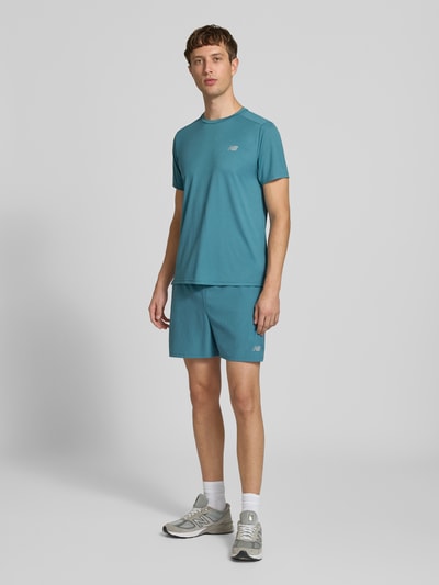Männermodel trägt Funktionsshirt mit Rundhalsausschnitt und Logo von New Balance in Blau, glatte Textur, Ganzkörperansicht von vorne, Rückenlänge bei Größe M 69 cm, Regular Fit.