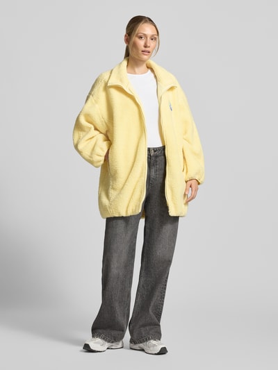 Frauenmodel trägt Oversized Jacke mit Stehkragen Modell 'Hoktown' von American Vintage in Gelb, Fleece, Reißverschluss, Logo-Patch, Ganzkörperansicht von vorne.