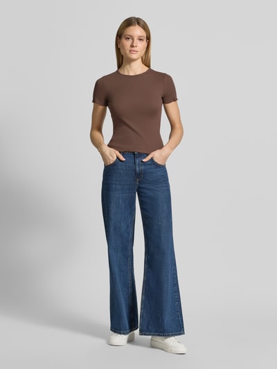 Modelka kobieca ma na sobie damski t-shirt z falistym brzegiem od Jake*s Casual, mieszanka bawełny z dodatkiem streczu, dopasowany krój, drobne prążkowanie, okrągły dekolt, długość tyłu w rozmiarze S: 52 cm, brązowy kolor, gładka struktura, pełen widok sylwetki z przodu.