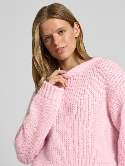 Frauenmodel trägt hellrosa Relaxed Fit Pullover im Chunky Knit Look Modell 'DORTHEA' von PIECES, grob gestrickt, Nahaufnahme Oberkörper.