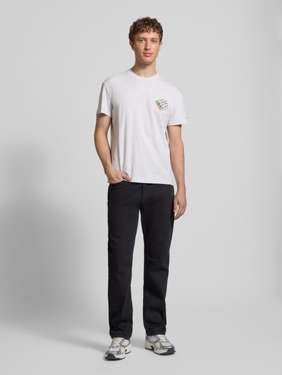 Männermodel trägt Regular Fit T-Shirt aus reiner Baumwolle von Tommy Jeans, unifarben, Label Print, Rundhals, Kurzarm, Jersey, Ganzkörperansicht von vorne.