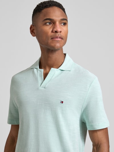 Männermodel trägt Regular Fit Poloshirt aus reiner Baumwolle von Tommy Hilfiger in melierter Optik, pastellgrün, Logo-Stitching, Nahaufnahme Oberkörper.
