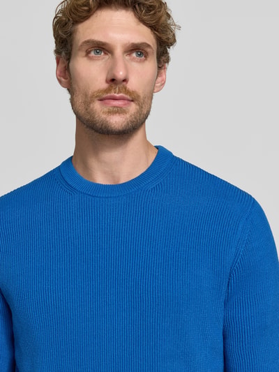Męski model nosi Regular Fit Strickpullover aus Baumwoll-Mix od MCNEAL, kolor niebieski, faktura prążkowana, okrągły dekolt, mieszanka bawełny, krój regular fit, elastyczne wykończenia, długość tyłu 65 cm, długość rękawów 56 cm, zbliżenie na górną część ciała.