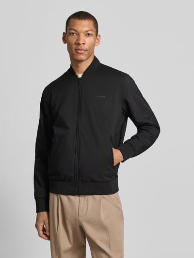 Männermodel trägt schwarze Bomberjacke mit Reißverschlusstaschen Modell 'MATTE' von CK Calvin Klein, Gerader-Schnitt, Ganzkörperansicht von vorne.
