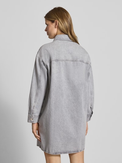 Frauenmodel trägt Loose Fit Jeanskleid aus reiner Baumwolle von Marc O'Polo Denim in grauer Denim-Optik mit Rückenpasse, Mini-Länge, Langarm, Manschette und Brusttasche, Ganzkörperansicht Rückansicht.