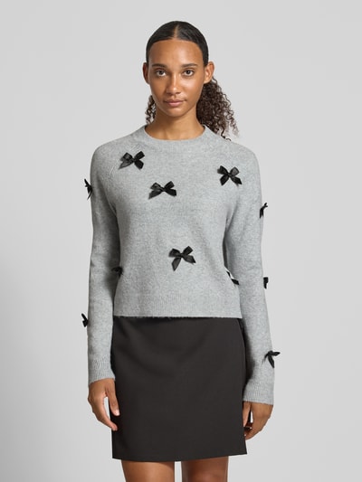 Frauenmodel trägt Regular Fit Pullover mit Raglanärmeln Modell 'NOELLE' von ONLY, hellgrau mit schwarzen Schleifen, Damen Pullover von ONLY, Ganzkörperansicht von vorne.