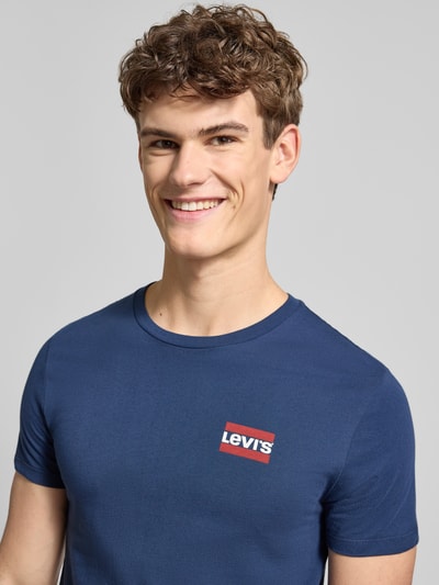 Męski model nosi T-shirt mit Label-Print im 2er-Pack od LEVI'S®, bawełna, krój slim fit, okrągły dekolt, nadruk z logo, zbliżenie na górę.