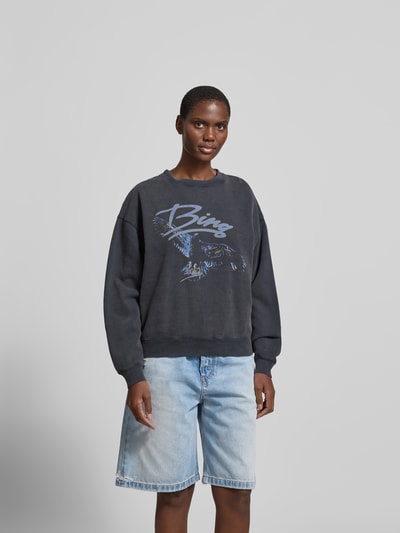 Frauenmodel trägt Regular Fit Sweatshirt mit Motiv-Print von Anine Bing, Reine Baumwolle, Rundhalsausschnitt, elastische Abschlüsse, Rückenlänge 59 cm bei Größe S, dunkle Farbe, dezenter Print, mittlere Struktur, Ganzkörperansicht von vorne.
