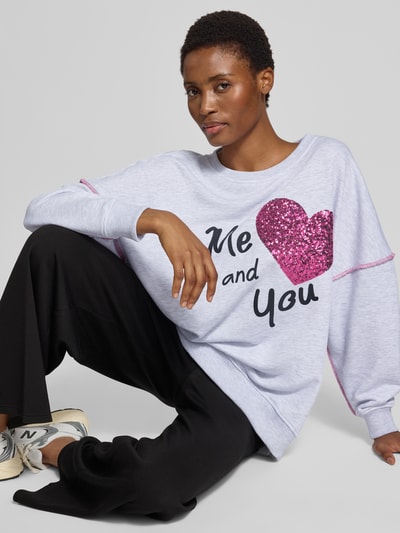 Frauenmodel trägt Oversized Fit Sweatshirt aus reiner Baumwolle von miss goodlife mit Paillettenbesatz, Statement-Print, elastische Abschlüsse, Grau, Schwarz, Pink, Ganzkörperansicht von vorne.
