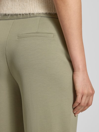 Frauenmodel trägt Stoffhose mit elastischem Logo-Bund von monari in hellem Grün, weiche Textur, Gesäßtasche sichtbar, Detailaufnahme Rückansicht, Material-Mix mit Viskose-Anteil.