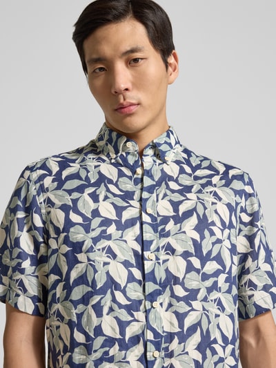 Mężczyzna nosi Regular Fit Freizeithemd aus Leinen mit Button-Down-Kragen od Christian Berg Men, wzór liści w odcieniach niebieskiego i bieli, czysty len, krój regular fit, guzikowa listwa, półrękaw, widok na górną część ciała od przodu
