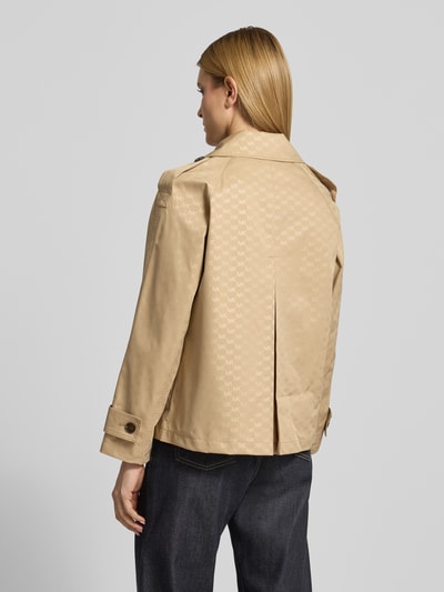 Frauenmodel trägt Trenchcoat mit Logo-Muster von MICHAEL Michael Kors, beiger Zweireiher, Reverskragen, Ärmelriegel, Rückenlänge 65 cm, Schulterbreite 48 cm, Brustweite 53 cm, Ärmellänge 57 cm, ganzkörperansicht Rückansicht.