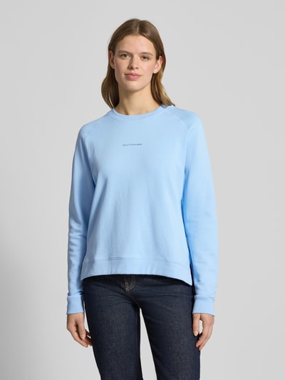 Vrouwenmodel draagt Regular Fit Sweatshirt uit pure katoen van Marc O'Polo Denim, effen lichtblauw, met labelopdruk, lange mouwen, ribdetails, sweatstructuur, ronde hals. Vooraanzicht bovenlichaam.