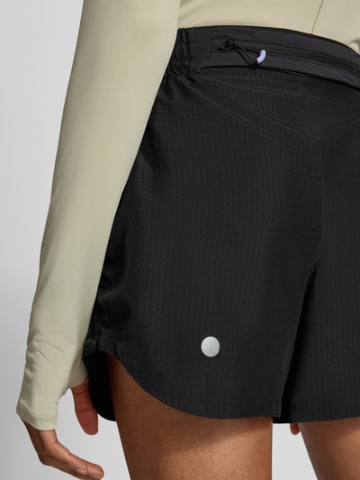 Frauenmodel trägt Shorts mit elastischem Bund Modell 'NAGINO' von ASICS TIGER, schwarze Farbe, Reißverschlusstasche, Detailaufnahme Hüfte