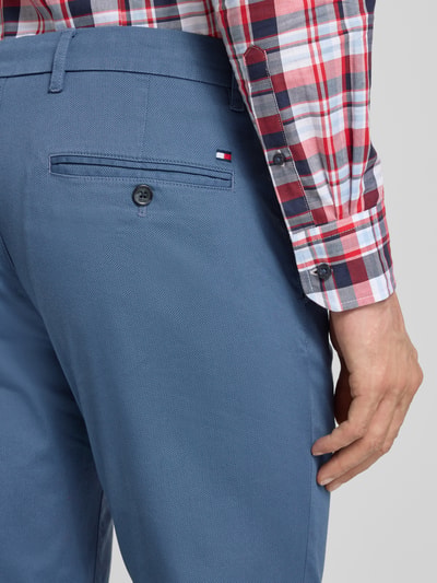 Männermodel trägt Slim Fit Chino aus Baumwoll-Mix Modell 'BLEECKER' von Tommy Hilfiger, niebieski, faktura gładka, detal tylnej kieszeni, Nahaufnahme Oberschenkel Rückansicht, kontekst: męskie spodnie chino, kieszenie, szlufki, uni kolor, label patch.