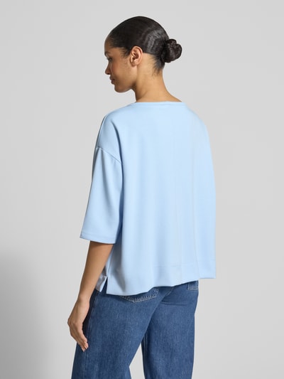 Frauenmodel trägt T-Shirt mit Rundhalsausschnitt und Logo von monari in Hellblau, Material-Mix mit Viskose-Anteil, Relaxed Fit, Ganzkörperansicht Rückansicht.