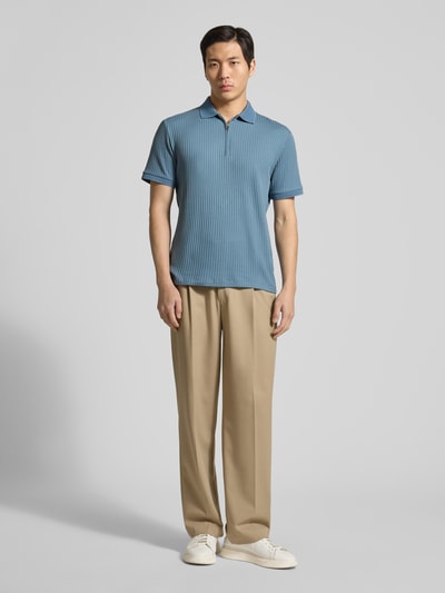 Męski model nosi Regular Fit Poloshirt mit Baumwoll-Anteil Modell 'FAVE' od SELECTED HOMME, kolor jednolity, krój regular fit, krótki zamek, kołnierz polo, krótkie rękawy ze ściągaczem, materiał prążkowany, zdjęcie całej sylwetki z przodu.